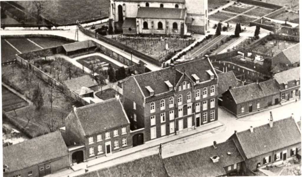 Foto vanaf hoogte van de voorgevel van het noviciaatsgebouw, met op de achtergrond de tuin en de kerk van Neeritter