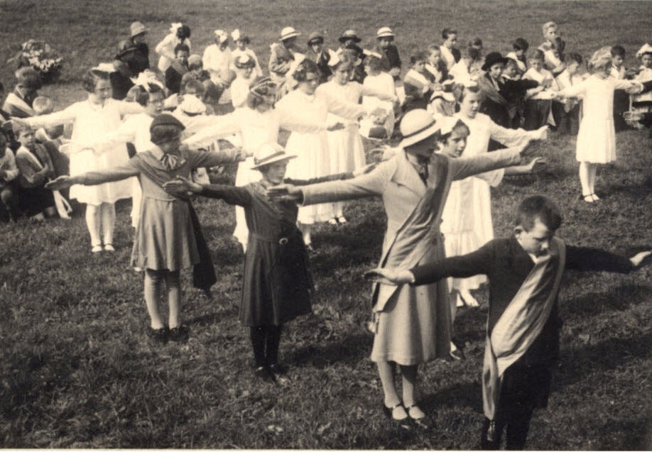 feestelijk uitgedoste kinderen staan in een weiland in gelid met de armen gespreid