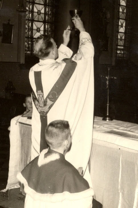 een priester in kazuifel van op de rug gezien aan het altaar heft de kelk omhoog