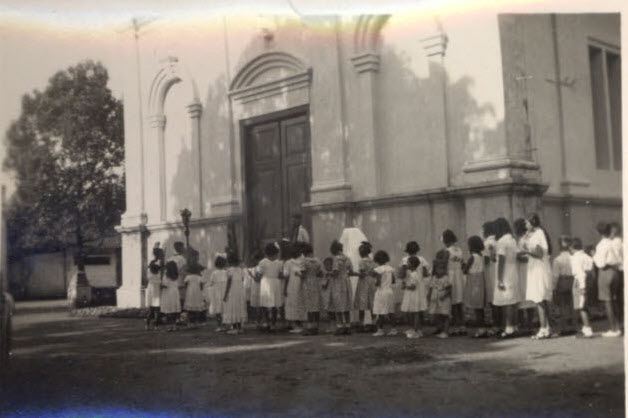Processie met kinderen voor de deur van een kerkgebouw.
