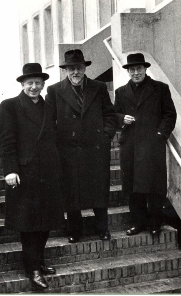 informele foto van drie kruisheren in clergy, overjas en hoed roken een sigaret op de treden van een hoge stoep