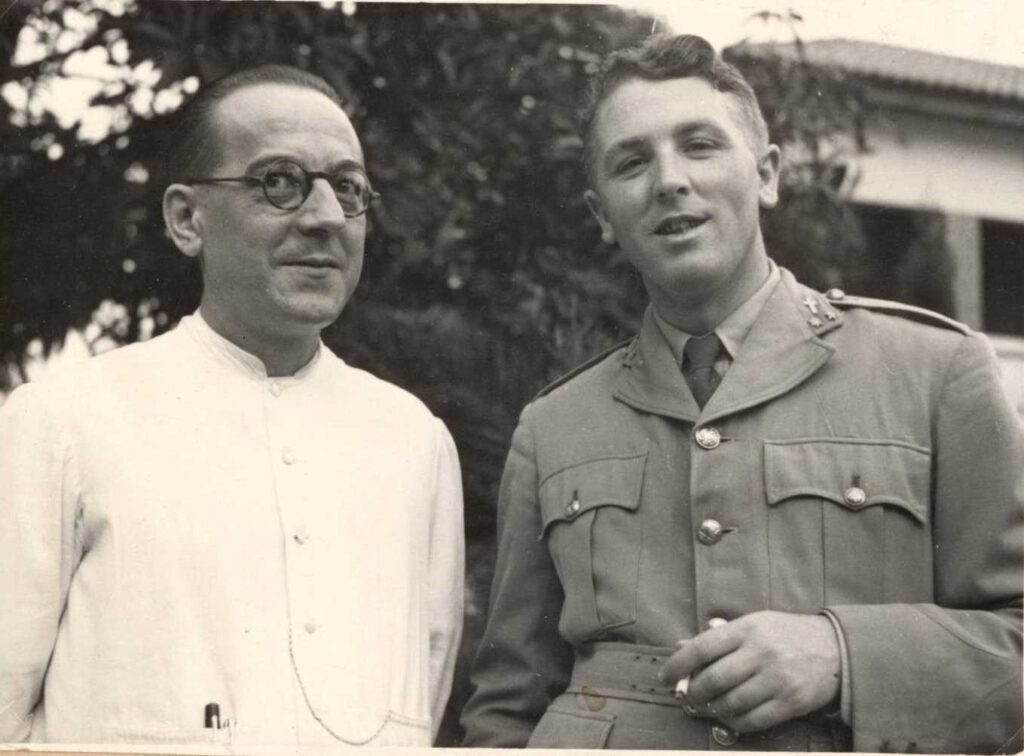 twee kruisheren, een in witte missionaristoog en een als aalmoezenier in legeruniform met sigaret in de hand