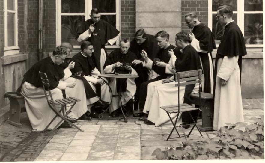 groep jonge kruisheren in habijt rond een klein tuintafeltje in kaartspel verdiept