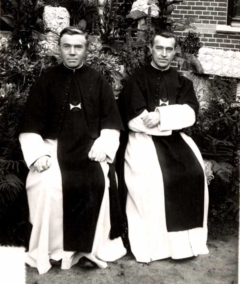 twee kruisheren in habijt zittend op een tuinbank