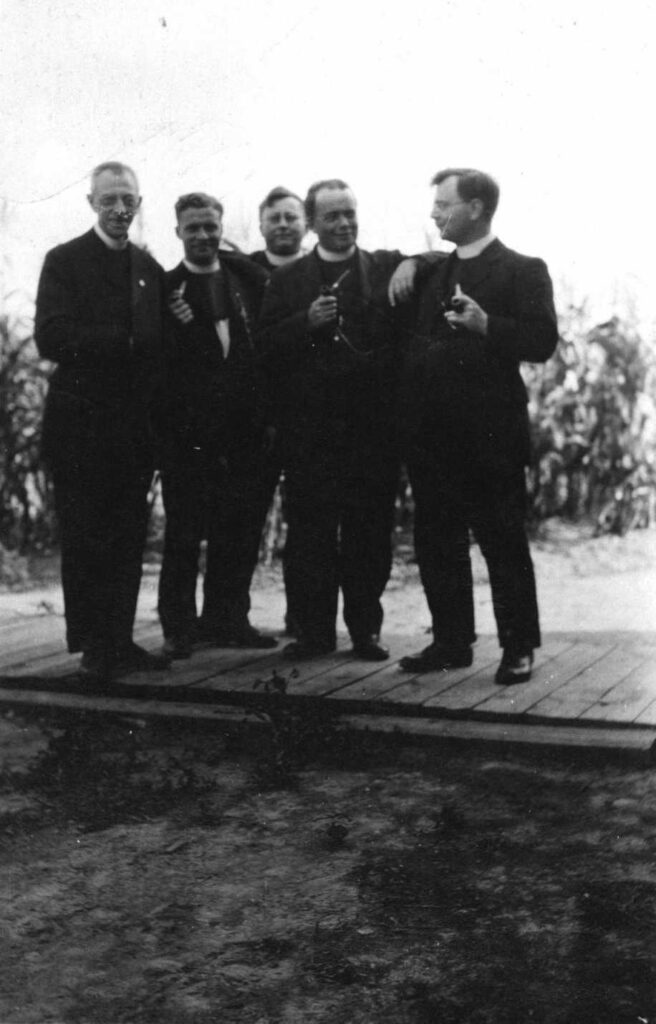 ontspannen groepsfoto van vijf kruisheren in clergy met pijp in de hand op een pad van planken