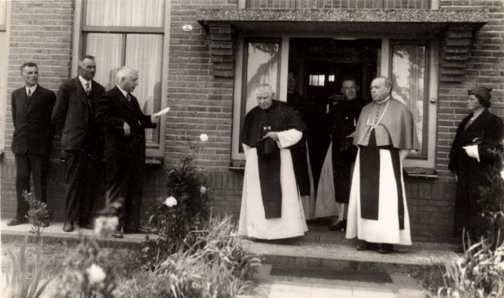 drie kruisheren in habijt in de voordeur worden toegesproken