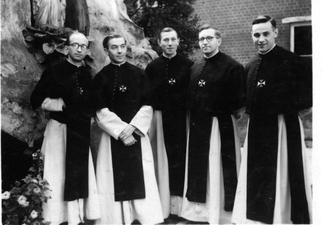 vijf jonge kruisheren in habijt staand voor een Lourdesgrot